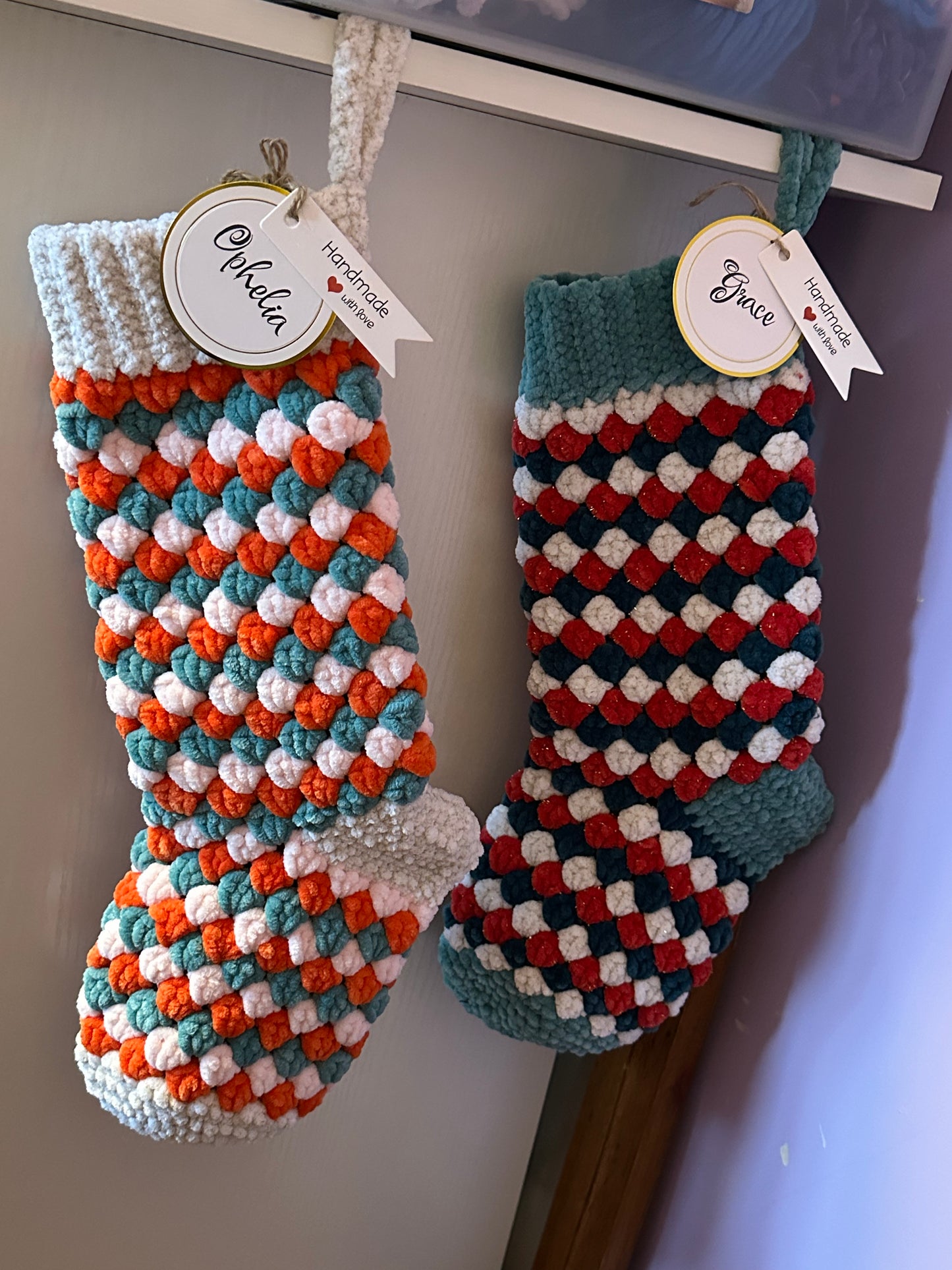 Two crocheted stockings with colorful patterns hanging on a white surface.