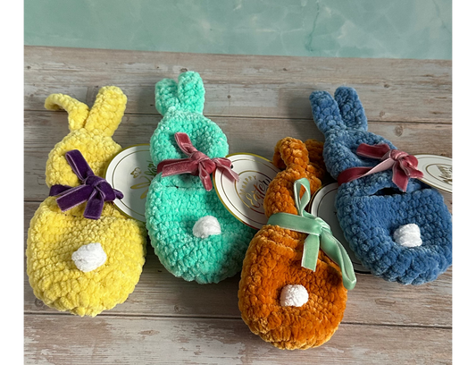Four colorful plush gift pouches shaped like bunnies on a wooden surface with a green background.
