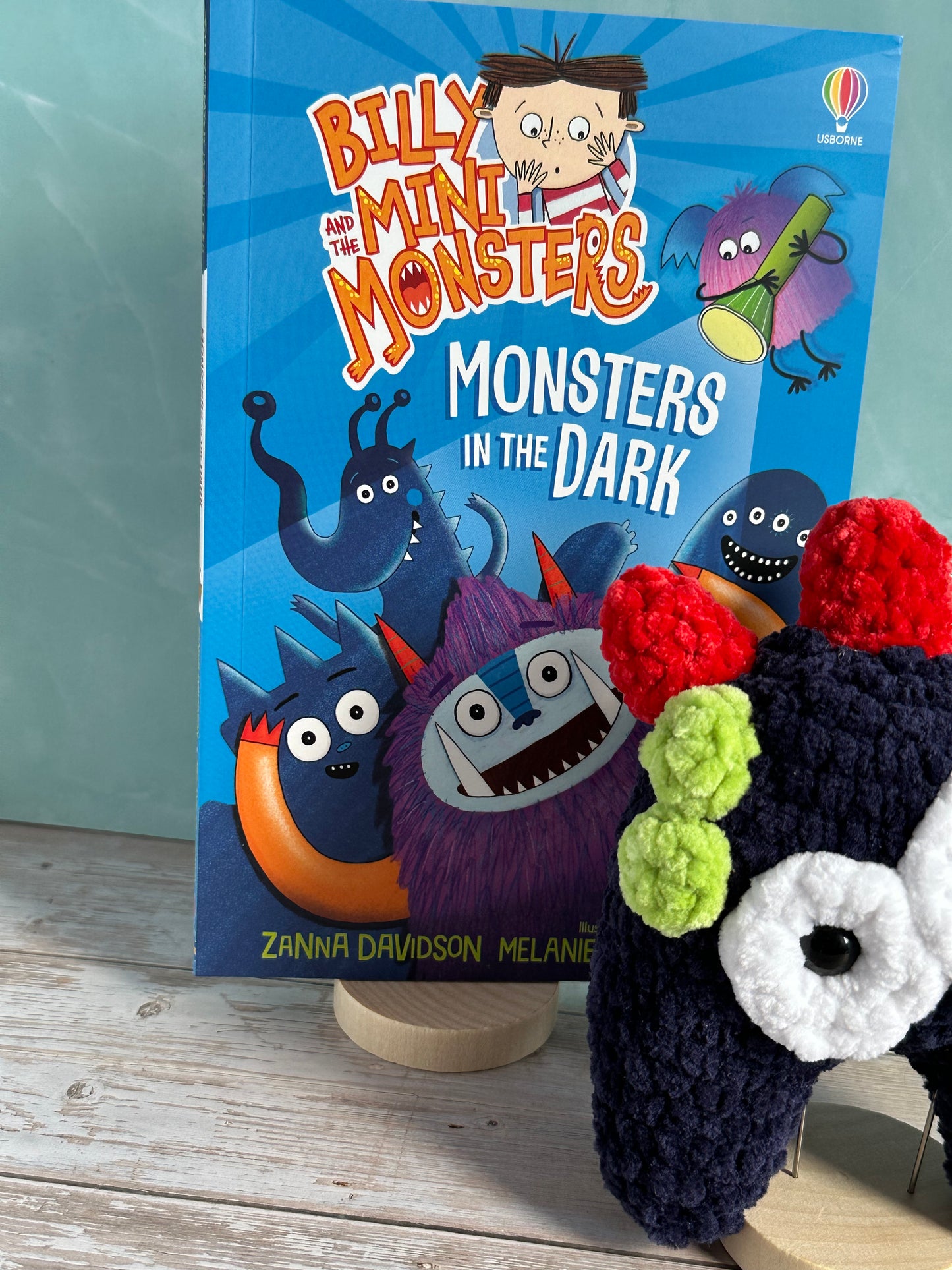 Navy Monster with Red horns in the foreground and a close up of the Billy and the Mini Monsters "in the Dark" Book