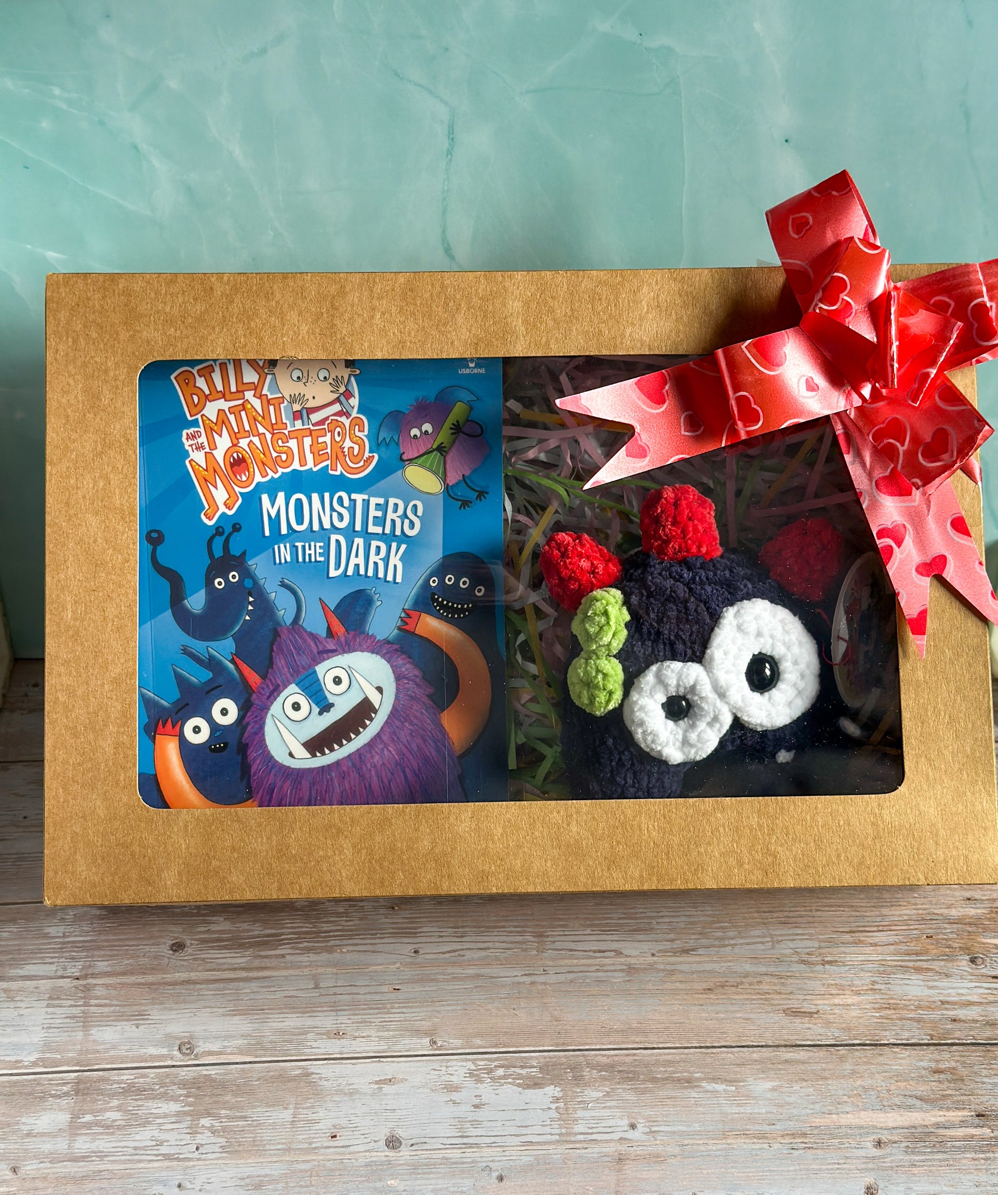 Navy Monster and Book presented in a cardboard box with a clear front showing off the contents and a gift bow on the top right hand corner.