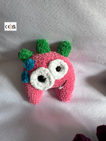 Pink crochet creature with green and blue accents on a light gray background