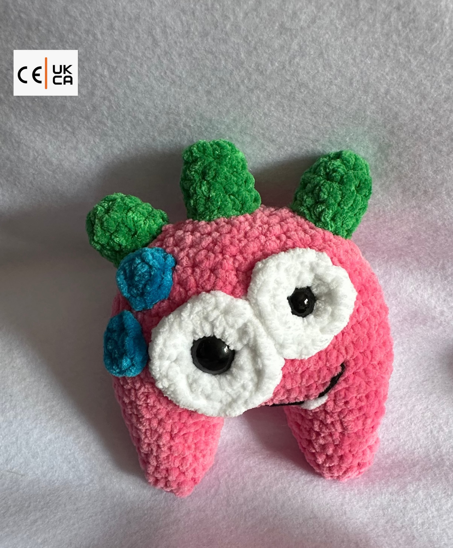 Crocheted pink monster with green and blue accents on a white background